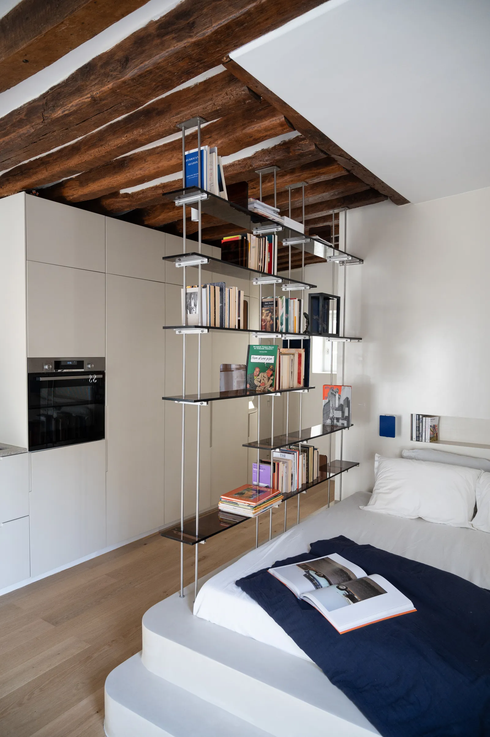 studio de 30 m2 à Paris 7e lit coffr dans le sol avec marches bibliothèque sparant la chambre de la cuisine poutres au...